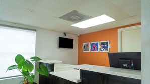 A reception area with a black reception desk, a potted plant, a flat-screen TV, and a wall with framed pictures. - Motel 6 Livingston, TX (Livingston)