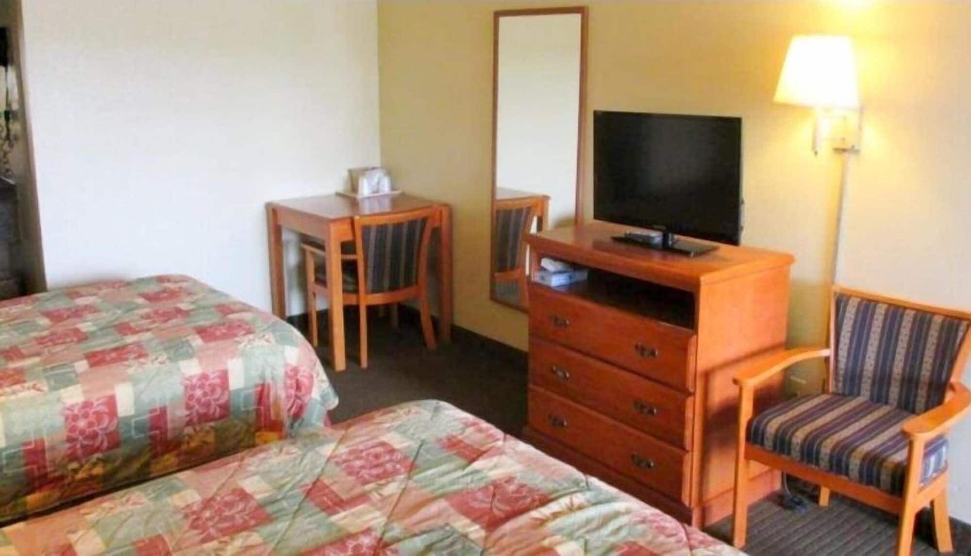 A hotel room with two beds, a desk, a dresser, a television, and a chair.