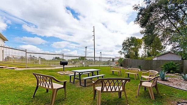 A fenced outdoor area with picnic tables and benches, a wooden fence, and a building in the background. - Motel 6 Livingston, TX (Livingston)