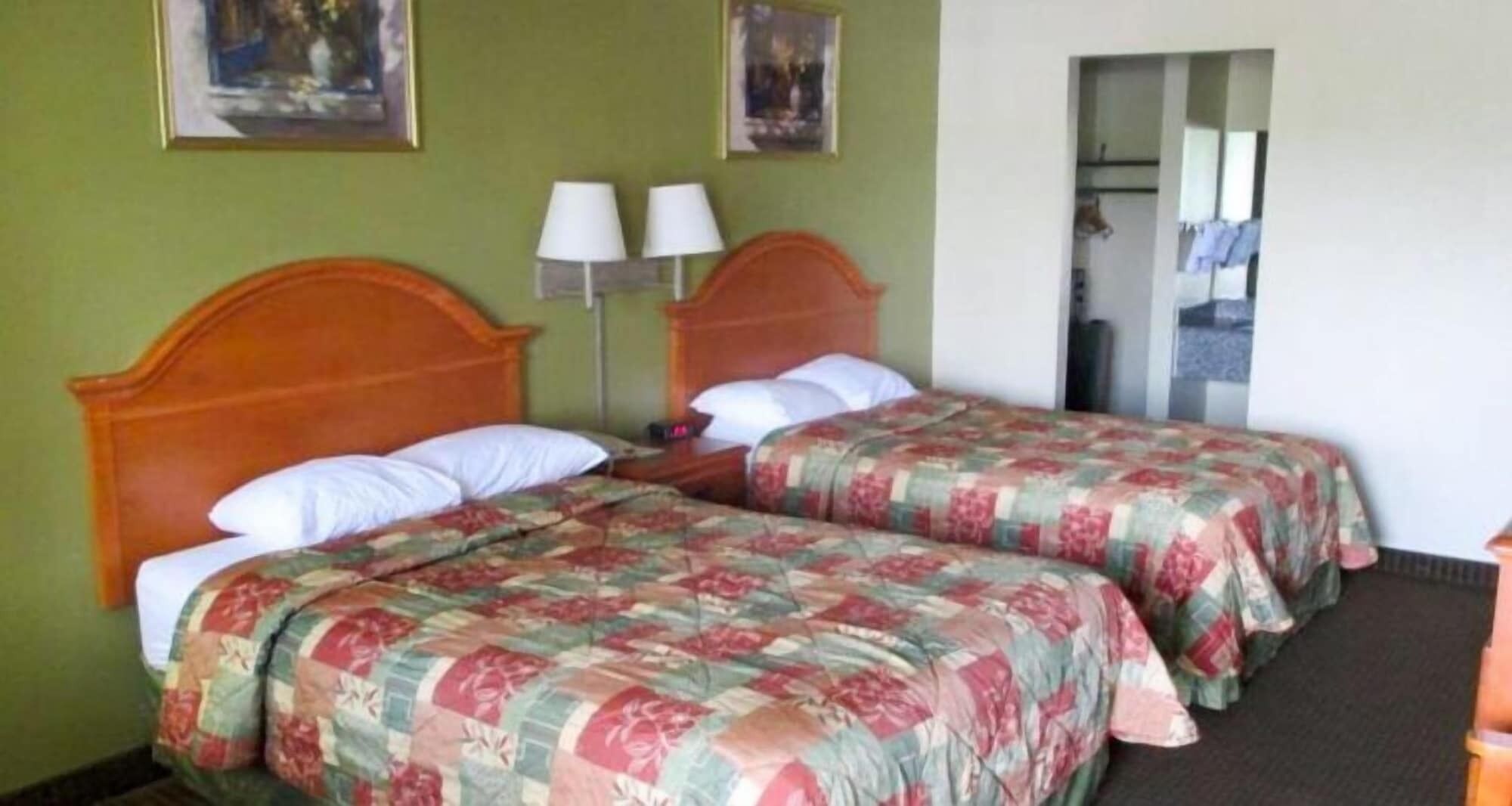 Une chambre d’hôtel avec deux lits, chacun doté d’une literie à motifs floraux, d’une tête de lit en bois et de deux lampes de chevet.