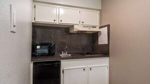 A compact kitchen with white cabinets, a microwave, a dishwasher, and a stainless steel sink. - Motel 6 Livingston, TX (Livingston)