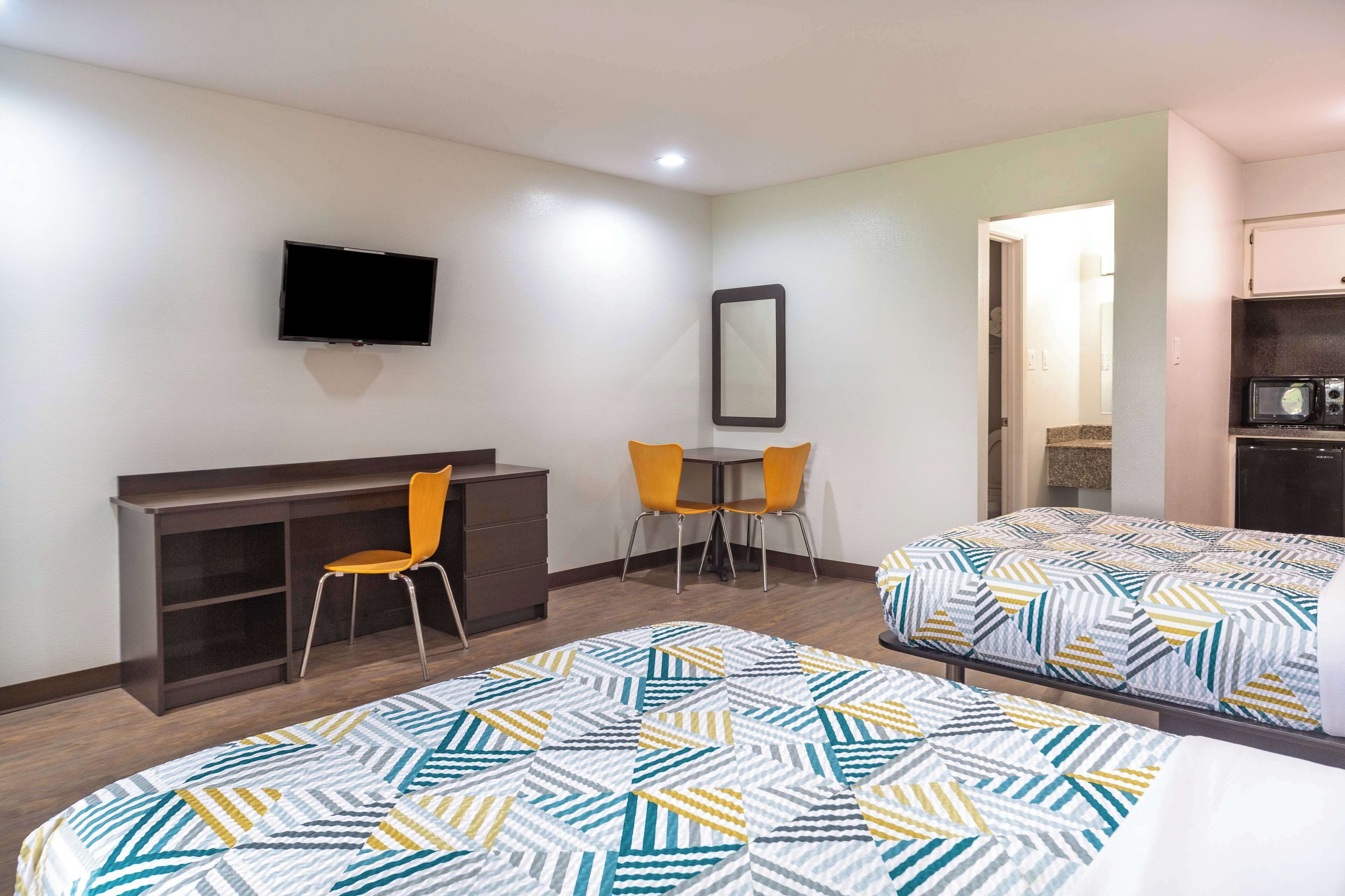 A hotel room with two beds, a desk, a chair, a TV, and a mirror.