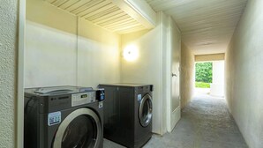 A laundry room with two washing machines, a wall-mounted dryer, and a door leading to a covered outdoor area. - Motel 6 Livingston, TX (Livingston)