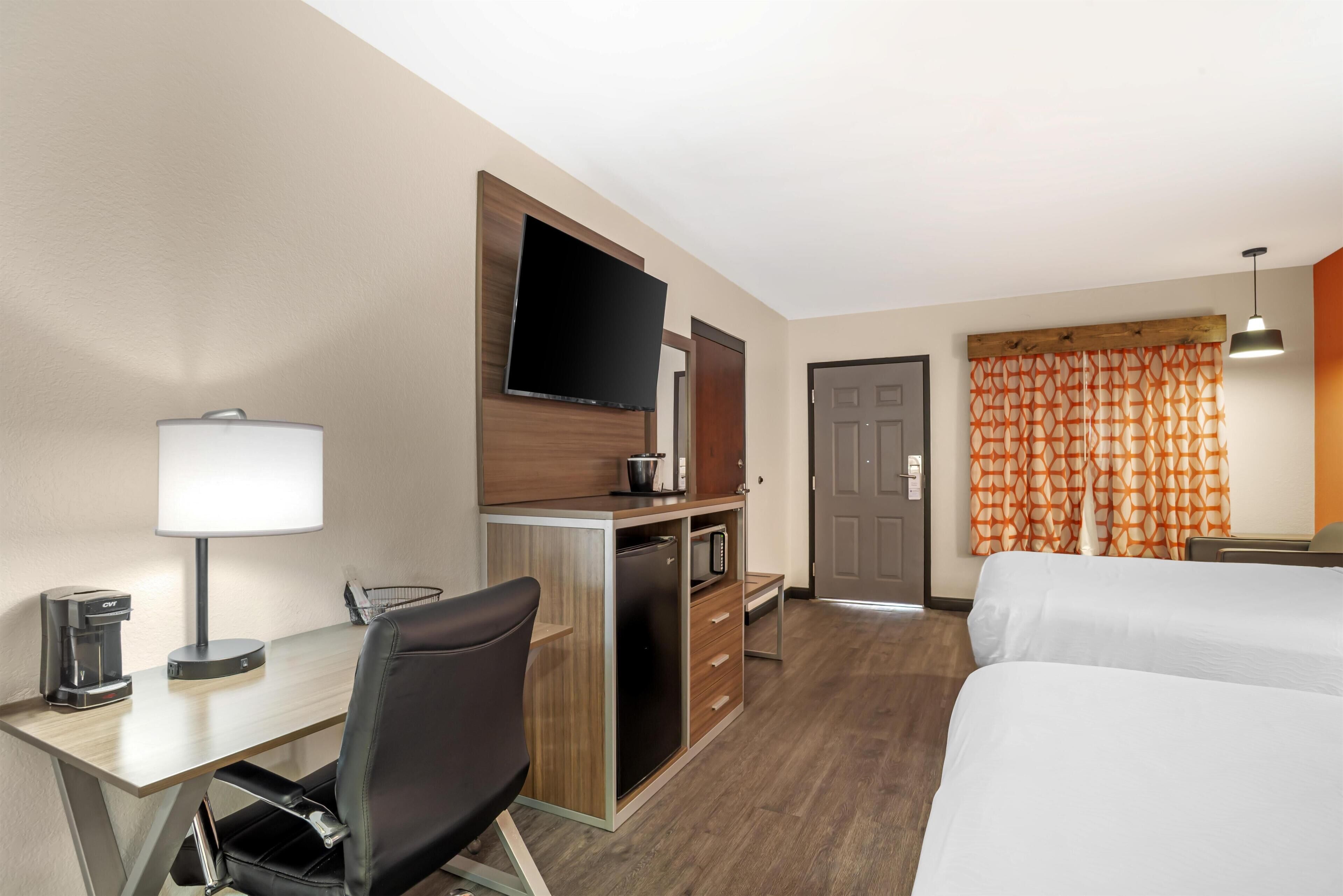 A hotel room with a desk, chair, TV, minibar, and two beds.