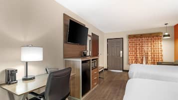 A hotel room with a desk, chair, TV, minibar, and two beds.