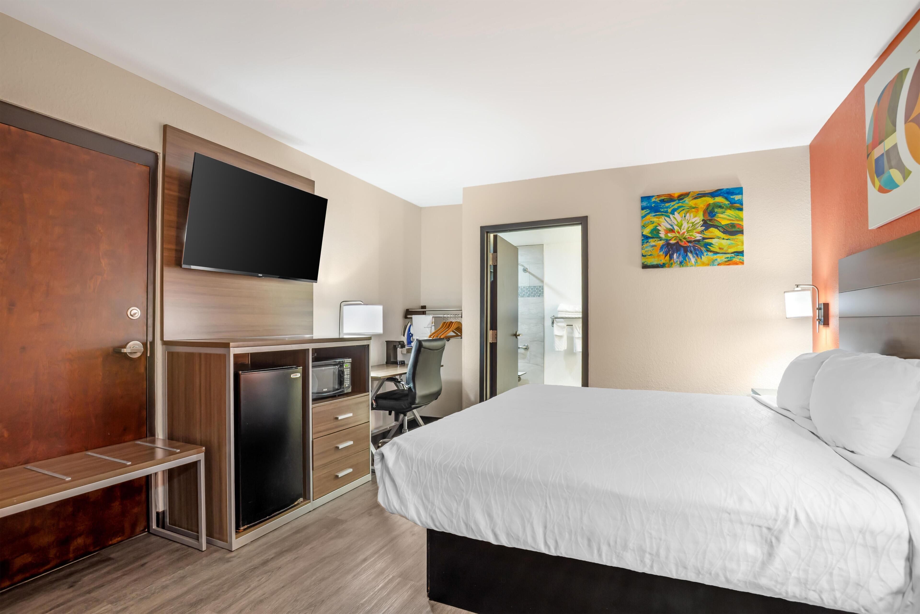 A hotel room with a bed, desk, chair, TV, and a door leading to a balcony.