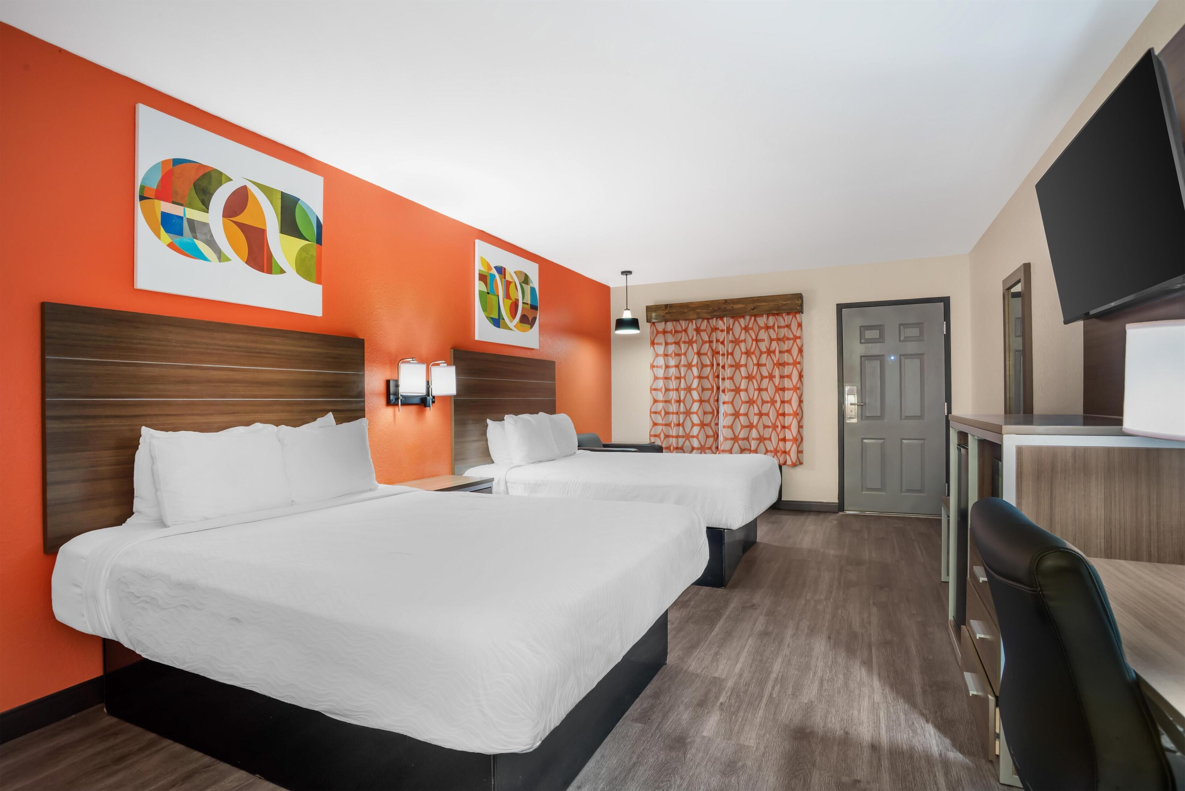 A hotel room with two beds, a desk, a TV, and artwork on the walls.