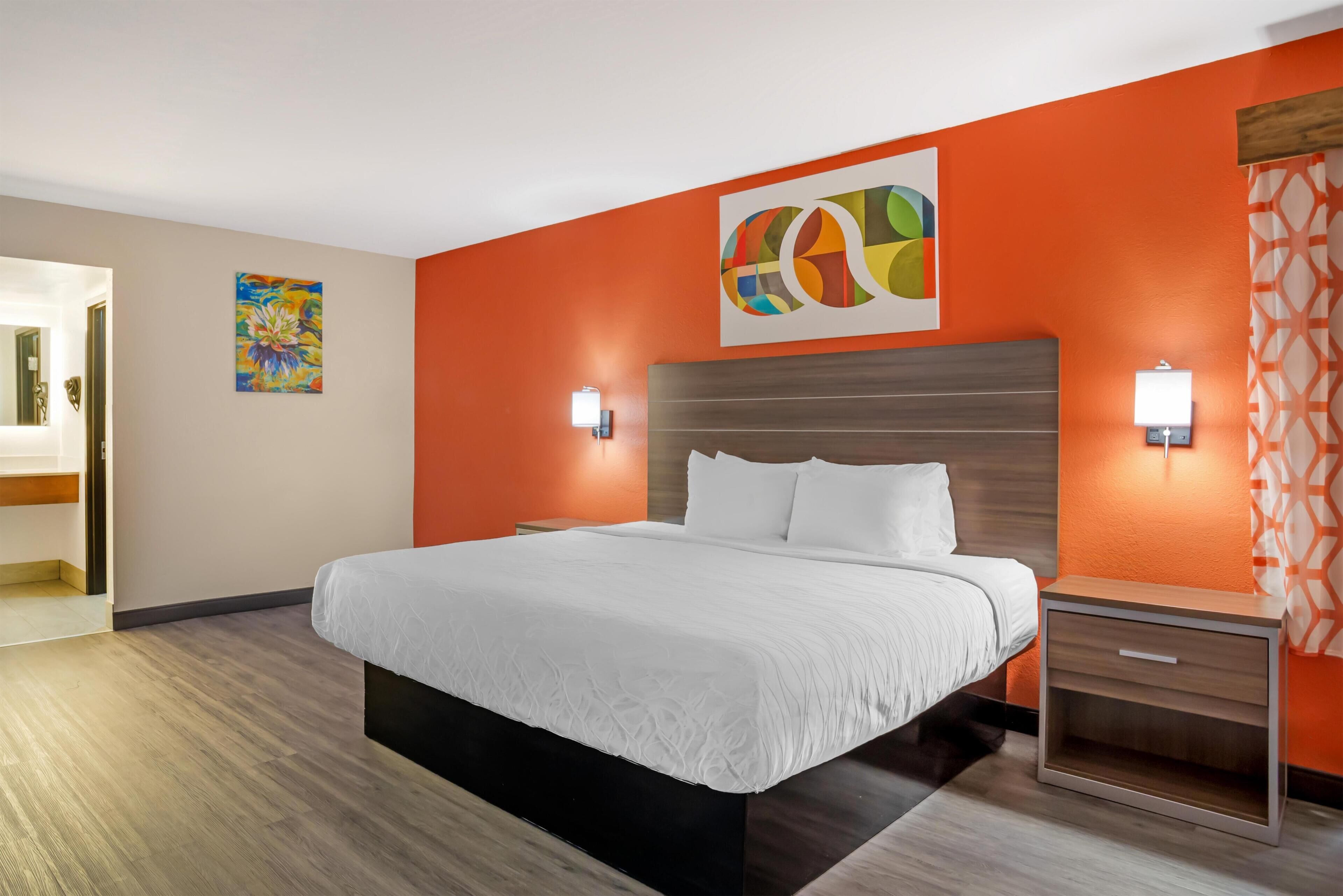 A hotel room with a large bed, two bedside tables, a wooden headboard, and two wall-mounted lamps.