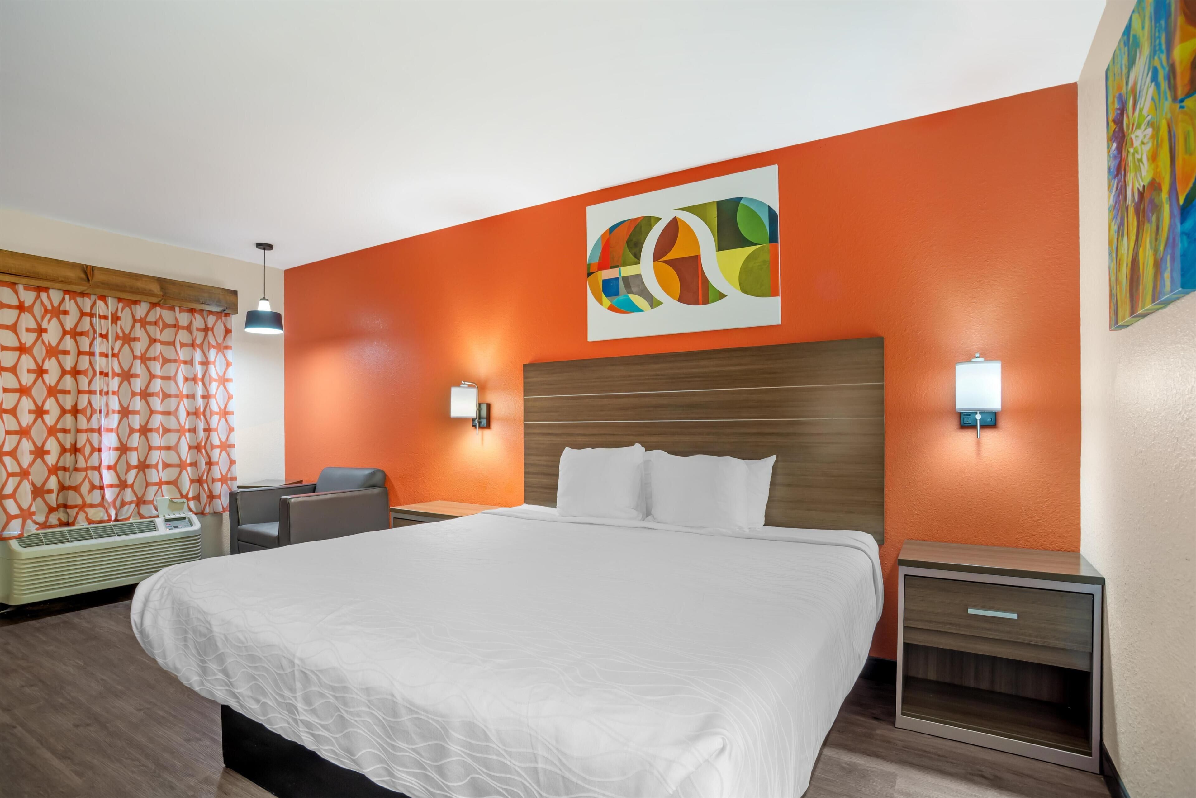 Habitació d'hotel amb un llit gran, dues taules de nit, un capçal de llit, una obra d'art penjada a la paret i una cortina amb dibuixos.