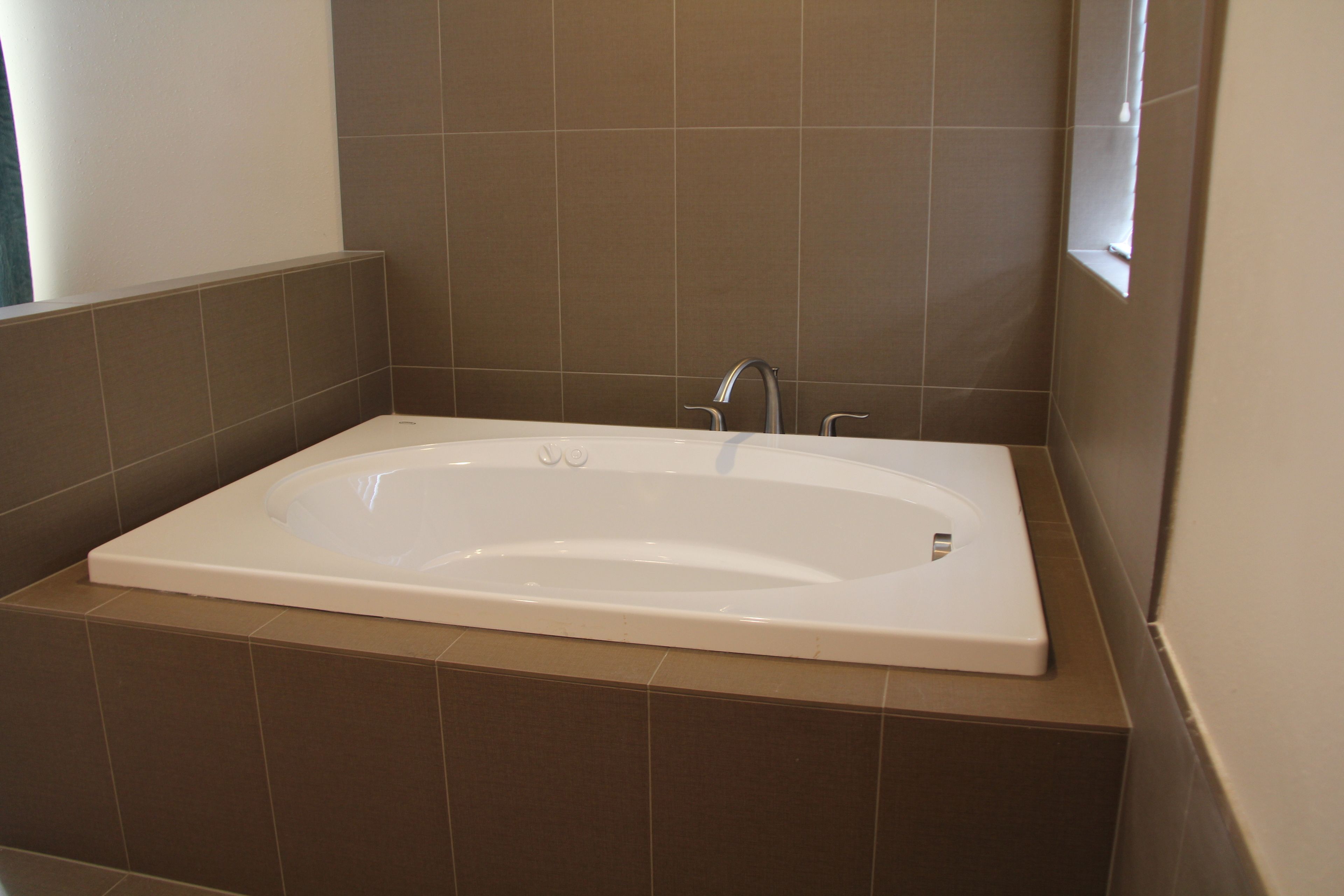 A modern bathroom with a freestanding bathtub, tiled walls, and a window providing natural light.
