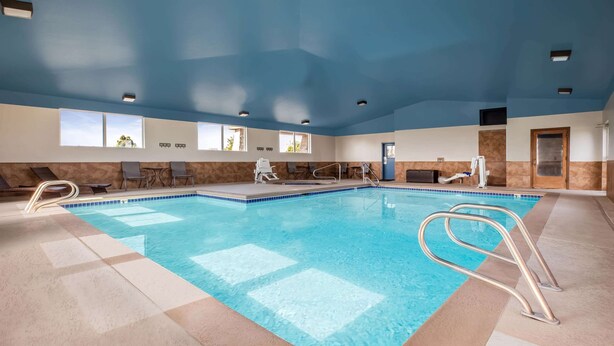 An indoor swimming pool with clear blue water, surrounded by lounge chairs and a sunbed.