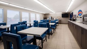 A restaurant with blue booths and tables, a kitchen area, and a large window.