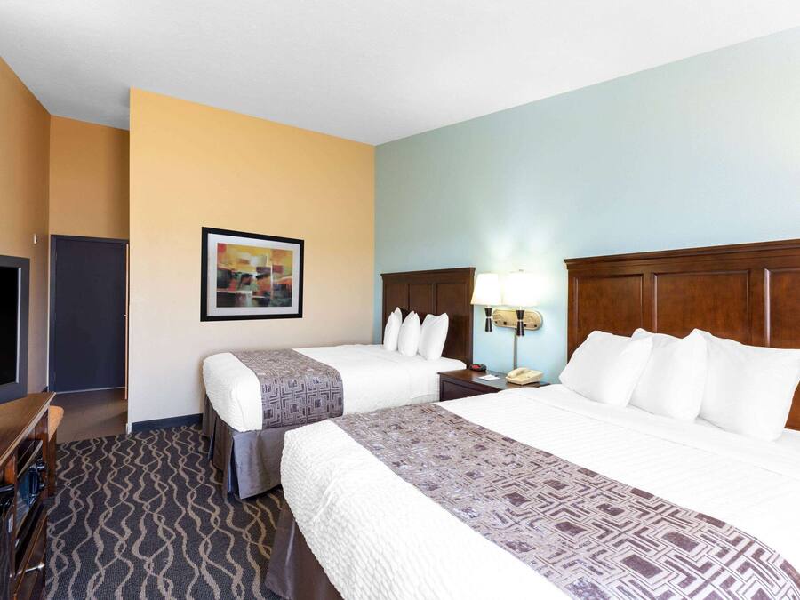 A hotel room with two beds, a TV, a desk, and a framed picture on the wall.