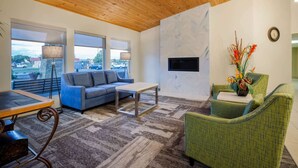 A modern living room with a wooden ceiling, a grey sofa, a green armchair, a coffee table, and a fireplace.