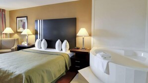 Habitación de hotel con una cama grande, dos mesitas de noche con lámparas, cabecero y un baño con bañera, además de una silla.