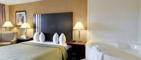 Habitación de hotel con una cama grande, dos mesitas de noche con lámparas, cabecero y un baño con bañera, además de una silla.