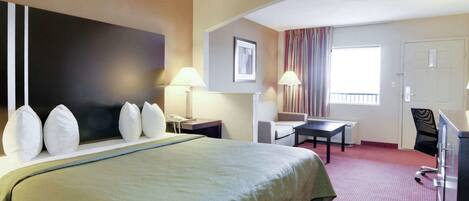 Une chambre d’hôtel avec un grand lit, un bureau, une chaise, un canapé, une télévision et une fenêtre avec des rideaux.