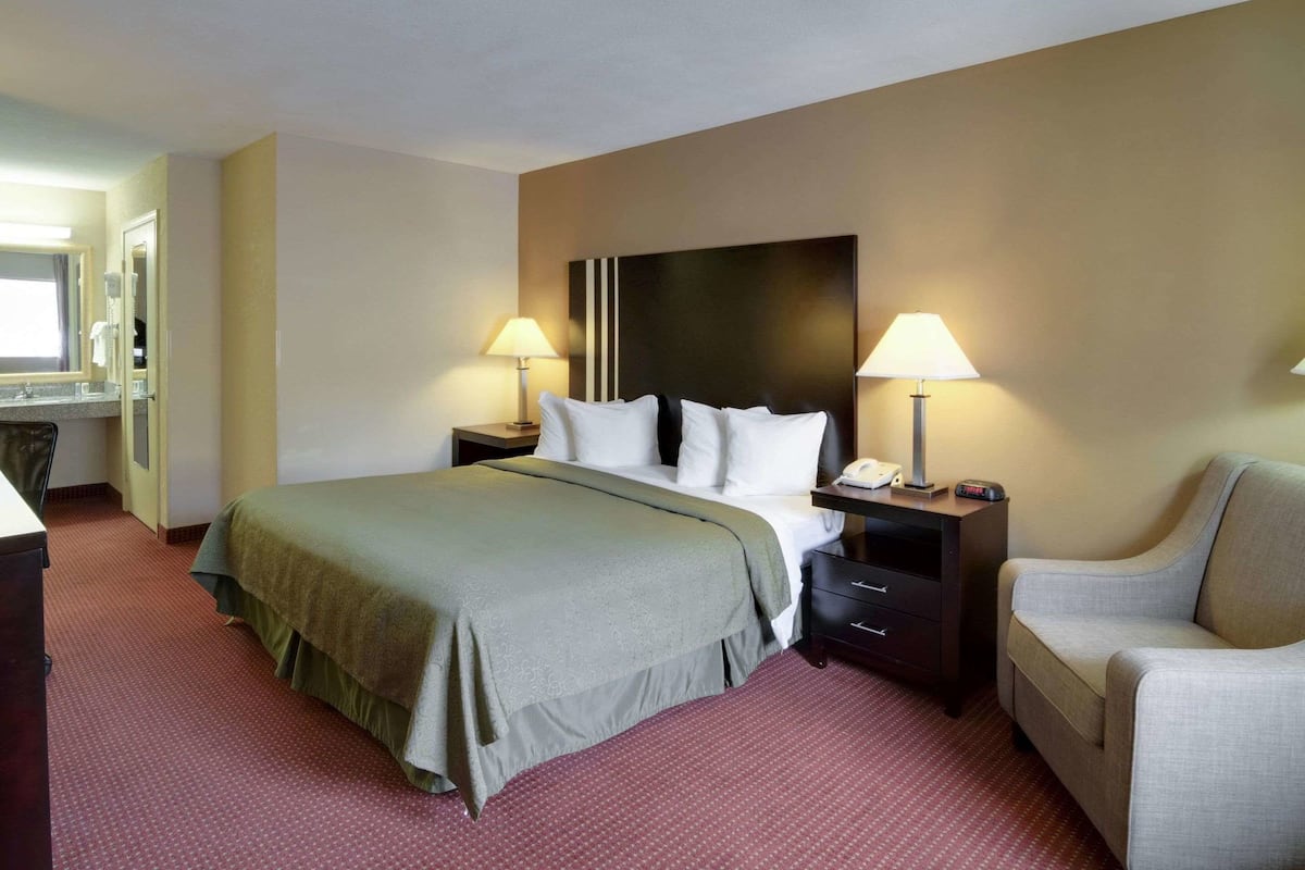 Een hotelkamer met een bed, twee nachtkastjes met lampen, een stoel, een bureau en een spiegel.
