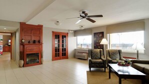 Un salón amplio con chimenea, ventilador de techo y un ventanal que proporciona luz natural.