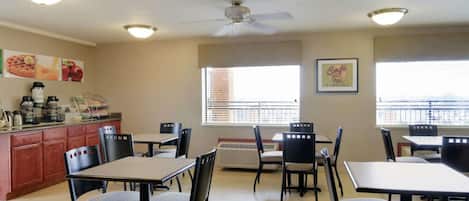 Un espace repas avec des tables et des chaises, un comptoir de cuisine équipé d’appareils électroménagers et un ventilateur de plafond.