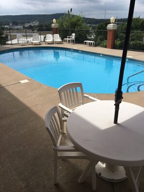 A swimming pool with white chairs and a table, surrounded by a fence and greenery. - Quality Inn & Suites Clarksville (Clarksville)