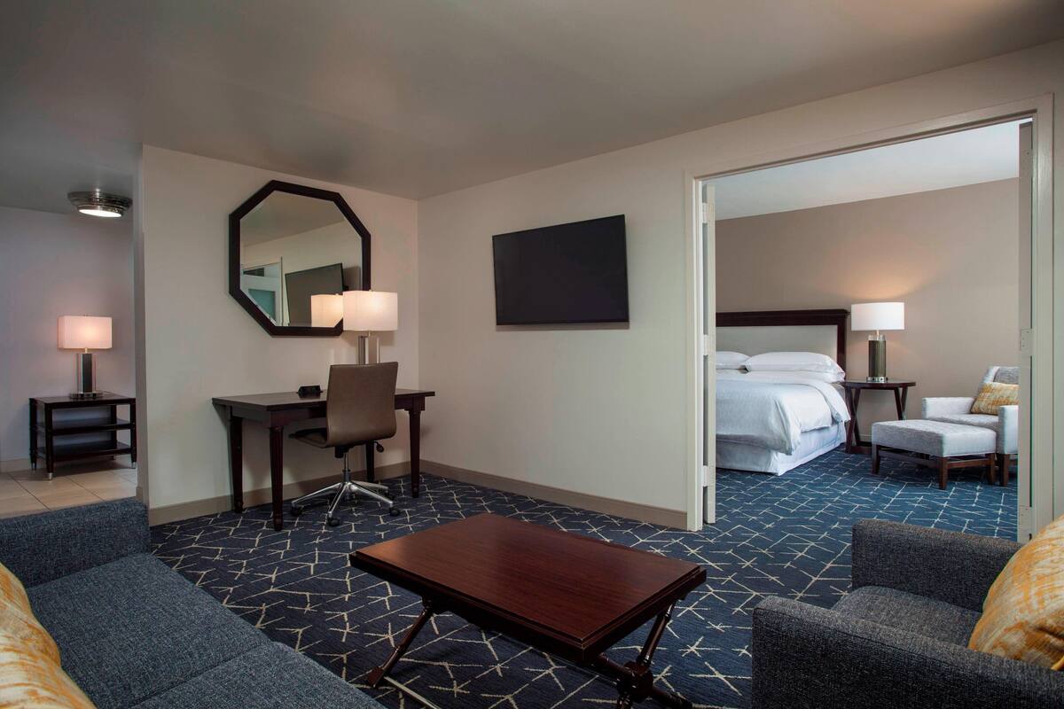 A hotel room with a desk, chair, sofa, and a bed.