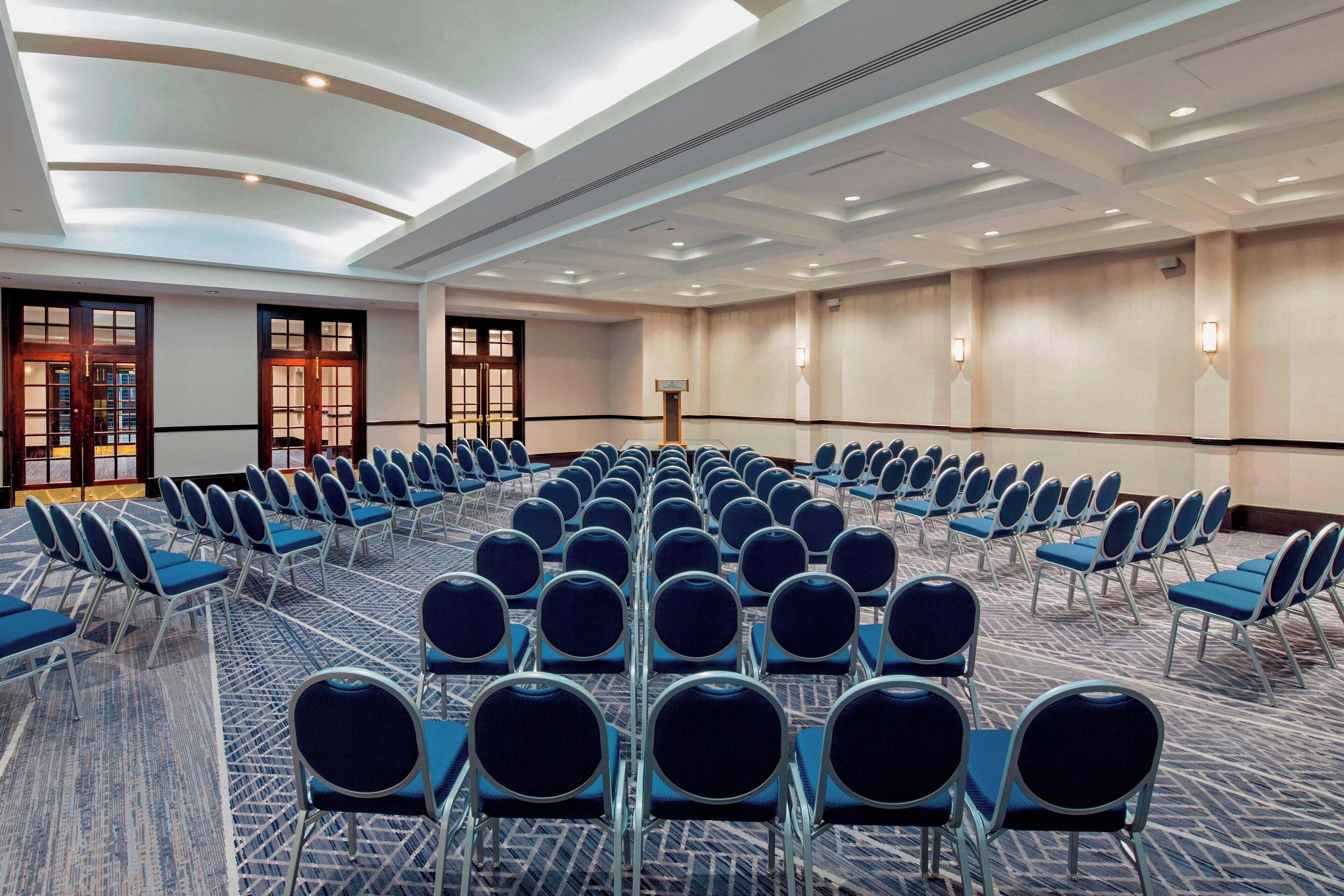 A conference room with rows of blue chairs, a patterned carpet, and a modern ceiling design.