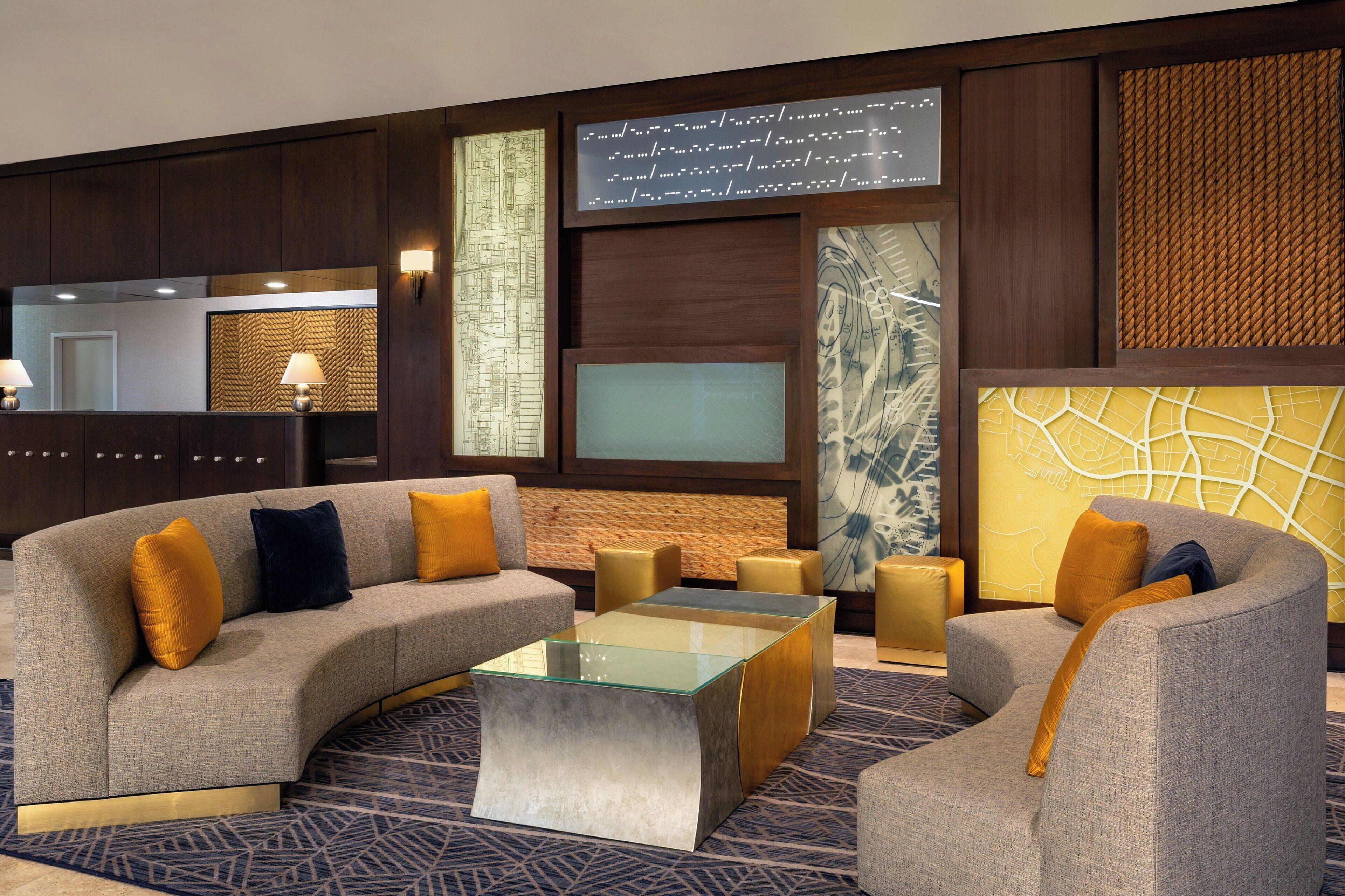 A modern hotel lobby with a curved sofa, a glass coffee table, and a seating area with armchairs and ottomans.