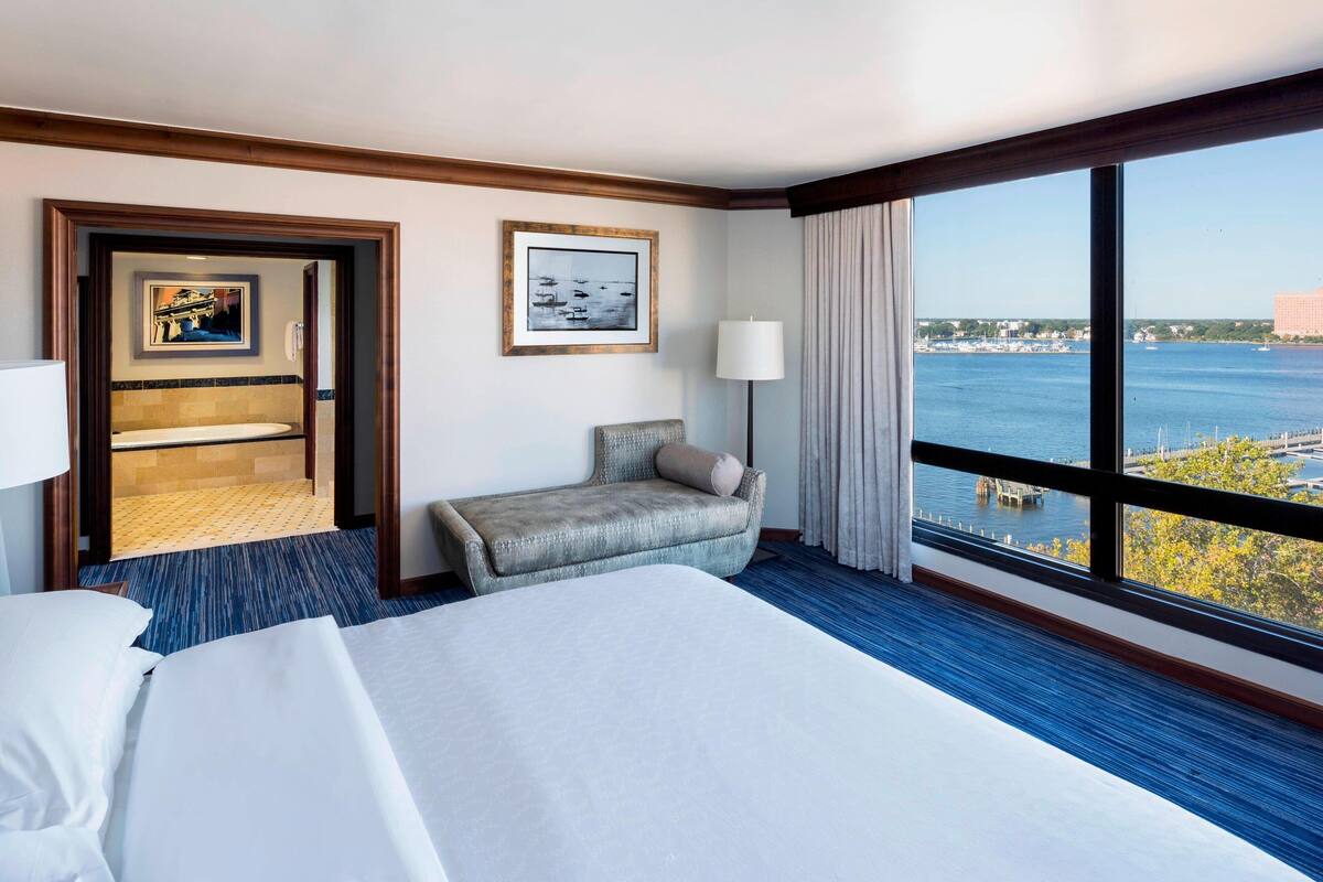 A hotel room with a large bed, a seating area, a view of the water, and a framed picture on the wall.