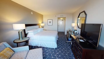 Quarto de hotel com cama, duas mesas de cabeceira com luminárias, televisão, cômoda e sofá.