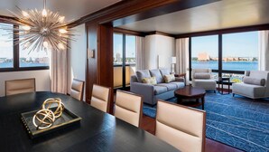 A modern hotel room with a dining area, a sofa set, and a view of the city and water. - Sheraton Norfolk Waterside Hotel (Norfolk)