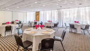 Un salón de conferencias con mesas redondas, sillas negras y manteles blancos.