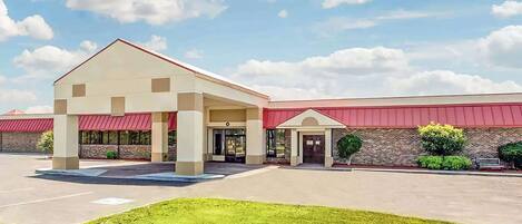 A building with a red roof and beige walls, featuring a covered entrance and a parking lot.