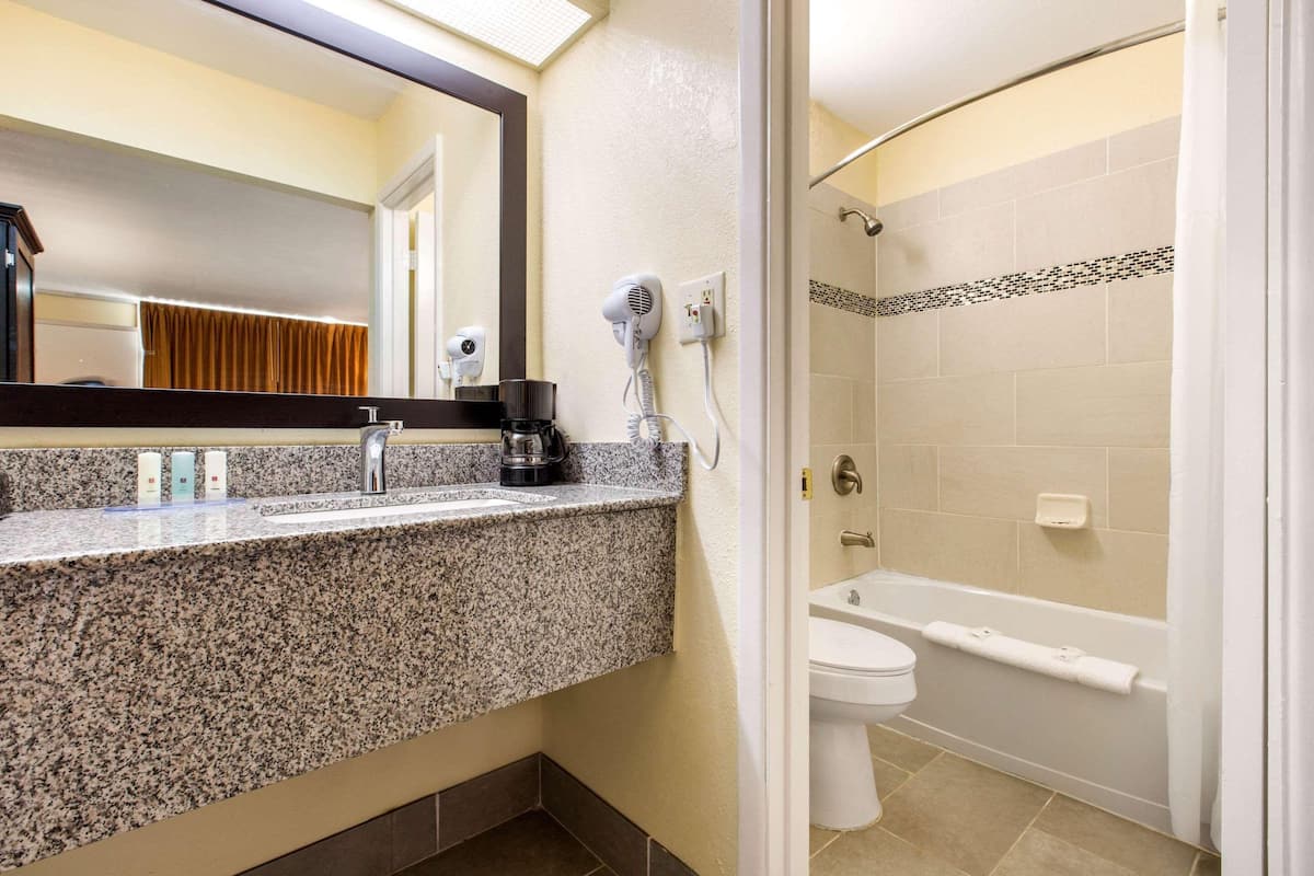 Un baño con encimera de granito, secador de pelo, cafetera, inodoro y bañera.