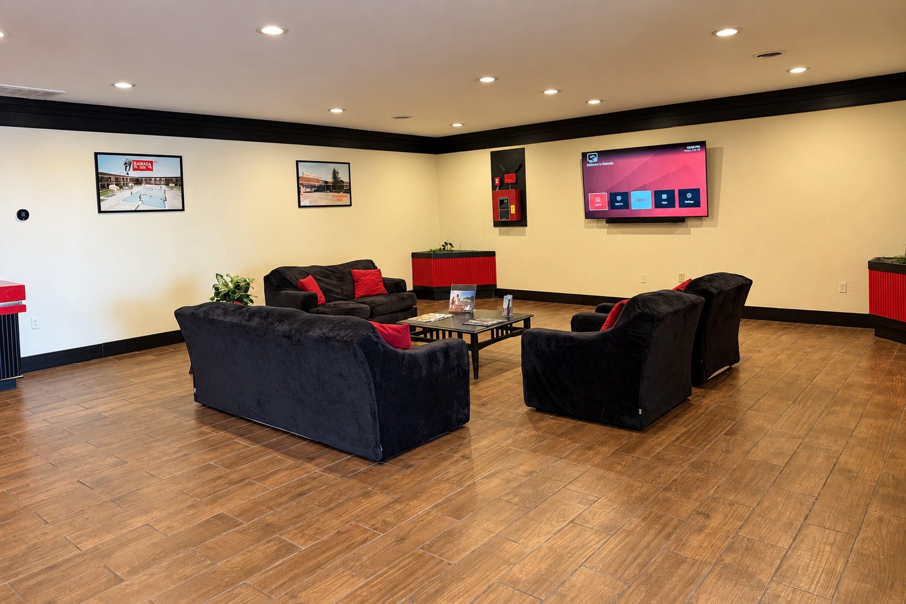 A modern lounge area with black sofas, a coffee table, and a flat-screen TV mounted on the wall.