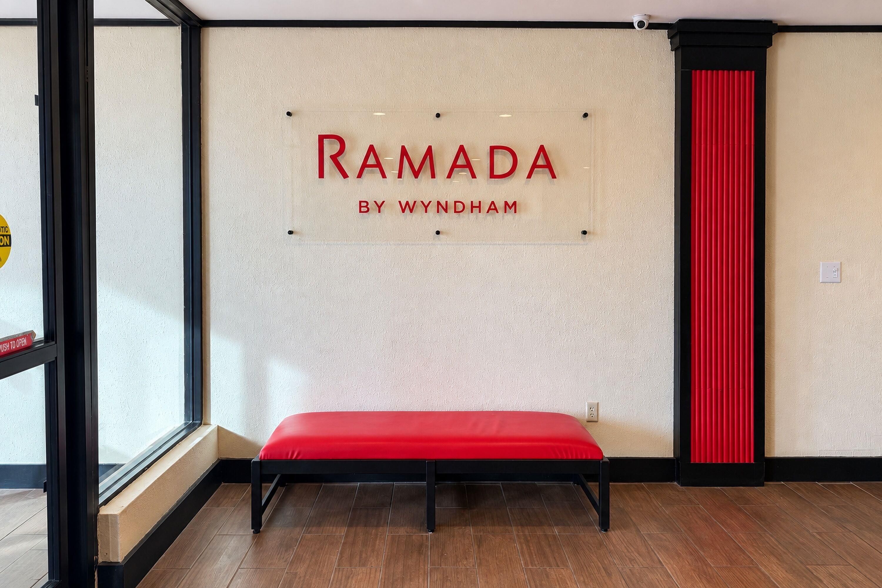 A wall with the text 'RAMADA BY WYNDHAM' and a red bench in a room with wooden flooring.