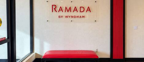 A wall with the text 'RAMADA BY WYNDHAM' and a red bench in a room with wooden flooring.