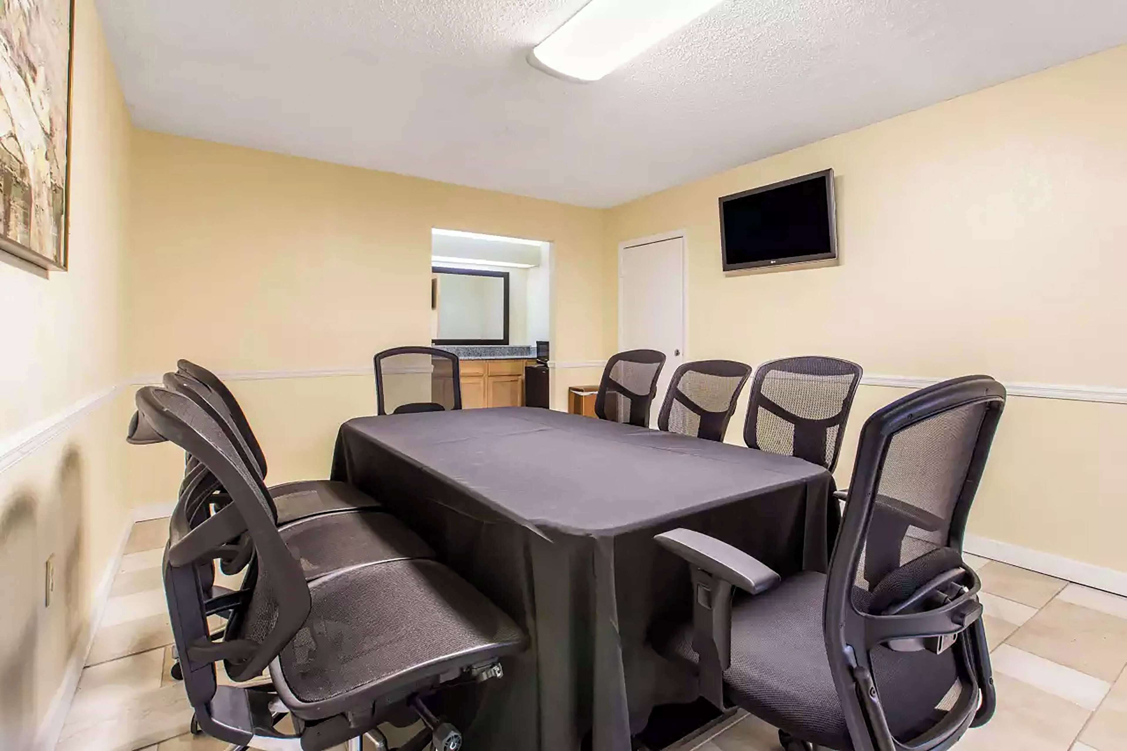 A conference room with a rectangular table, six office chairs, a flat-screen TV, and a door.