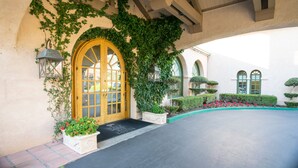 Una entrada de edificio con puerta de madera, una linterna y una maceta con flores.
