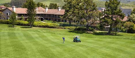A golf course with a clubhouse and residential buildings in the background.