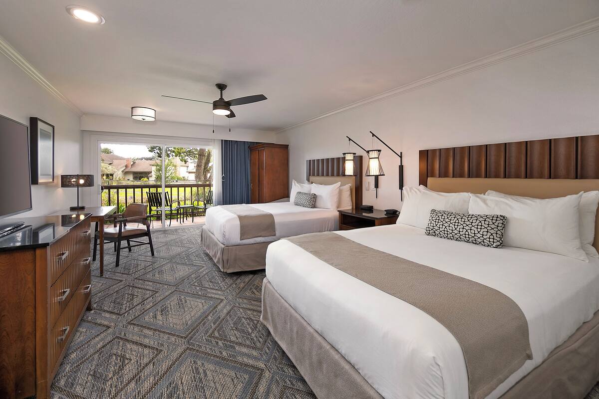 Quarto de hotel com duas camas, televisão, escrivaninha e varanda com vista.