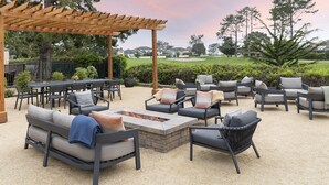 Un área de patio al aire libre con diversas opciones de asientos, incluyendo sofás y sillones, organizados alrededor de un hogar para la chimenea.