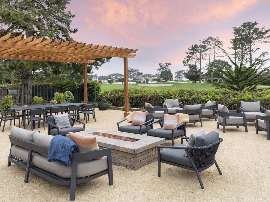 Un espace extérieur aménagé en terrasse, doté de différents types de sièges, notamment des canapés et des fauteuils, disposés autour d’un foyer central.