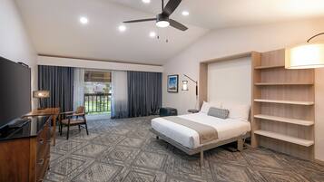A modern hotel room with a bed, desk, chair, and a ceiling fan.