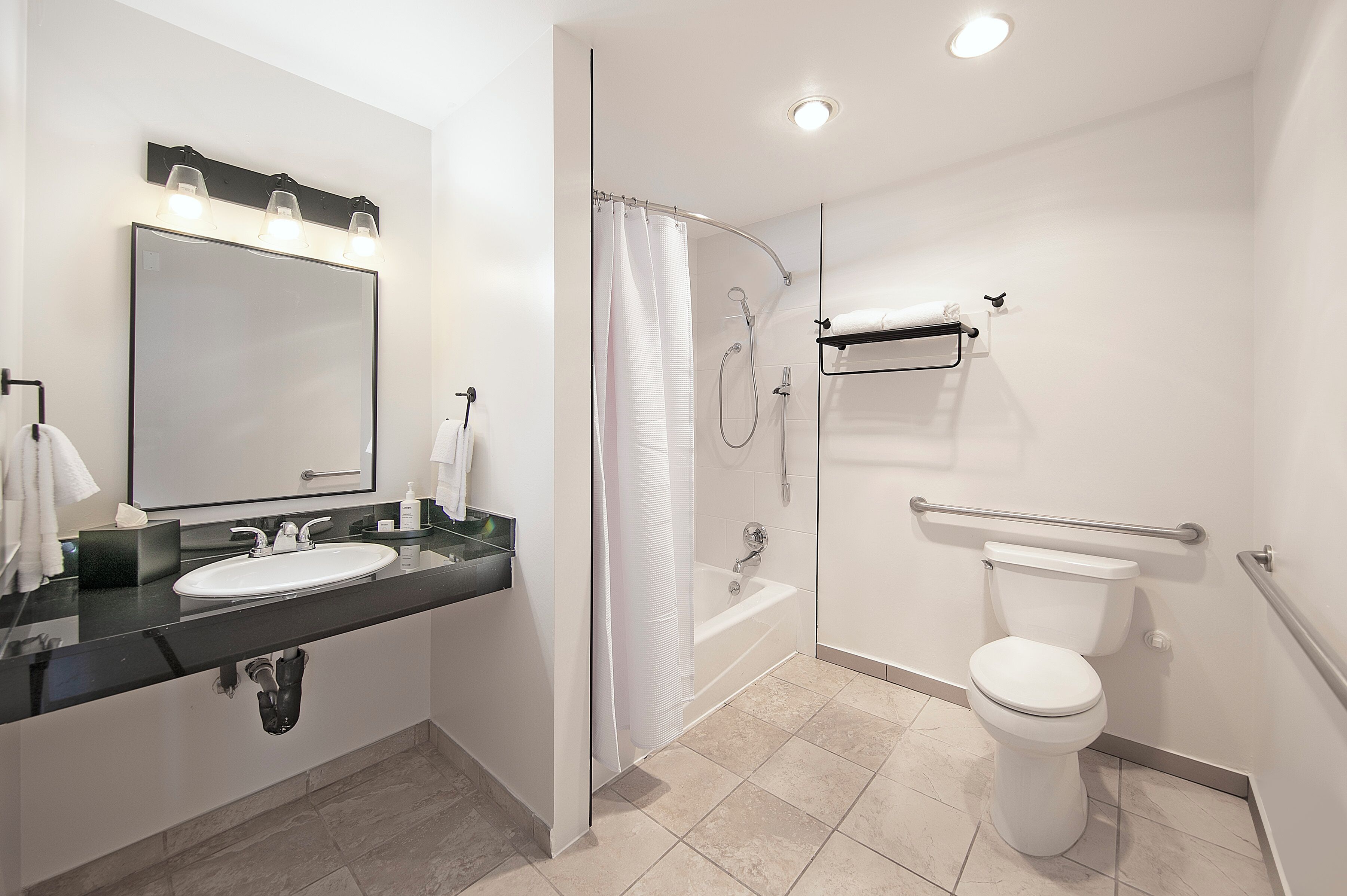 Une salle de bain moderne avec un grand miroir, un lavabo, une douche et des toilettes.