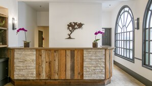 A reception area with a wooden reception desk, stone wall, and a large arched window. - Half Moon Bay Lodge (Half Moon Bay)
