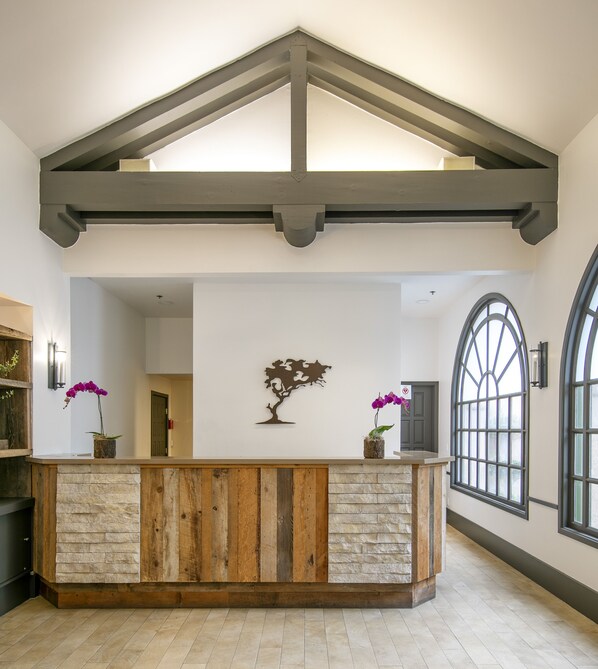 A reception area with a wooden reception desk, stone wall, and a large arched window. - Half Moon Bay Lodge (Half Moon Bay)