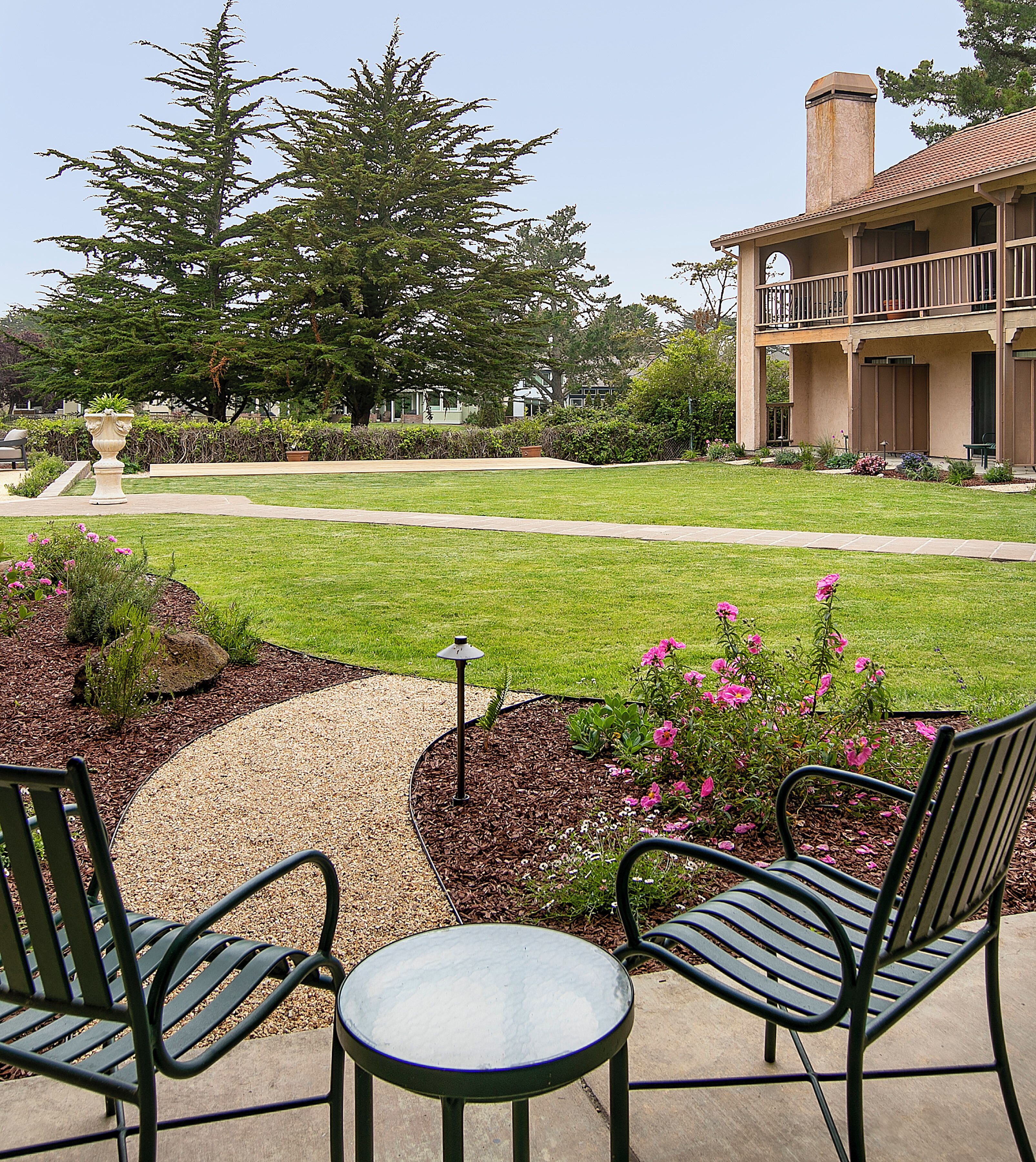 A patio area with two metal chairs and a small table, surrounded by a garden with various plants and flowers.
