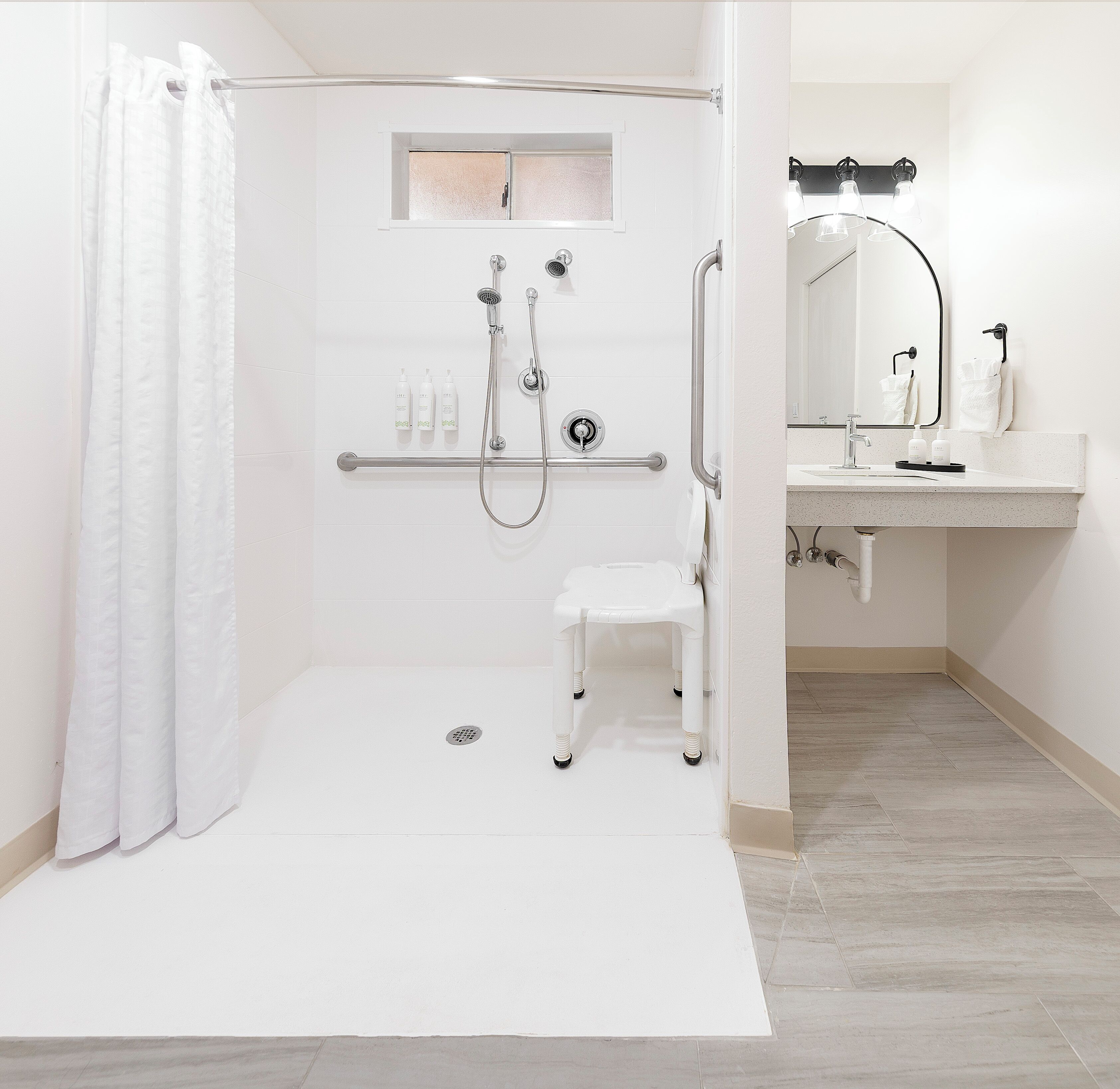 A modern bathroom with a walk-in shower, grab bar, and a small white stool.