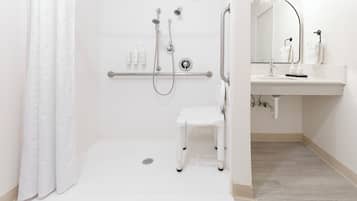 A modern bathroom with a walk-in shower, grab bar, and a small white stool.